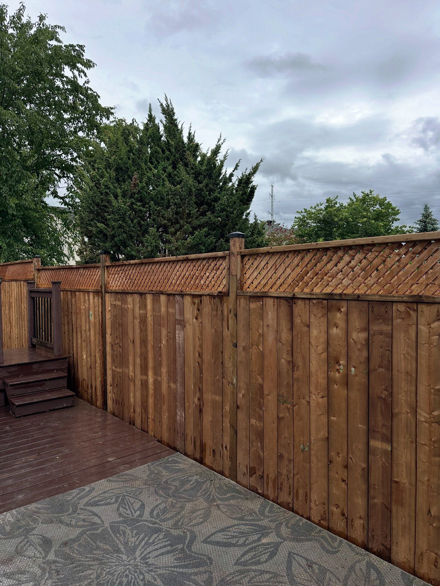 New wood privacy fence with a lattice top running along a backyard deck