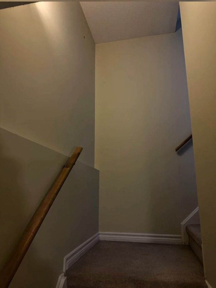 Basement stairwell with repaired, freshly painted walls and a wood handrail