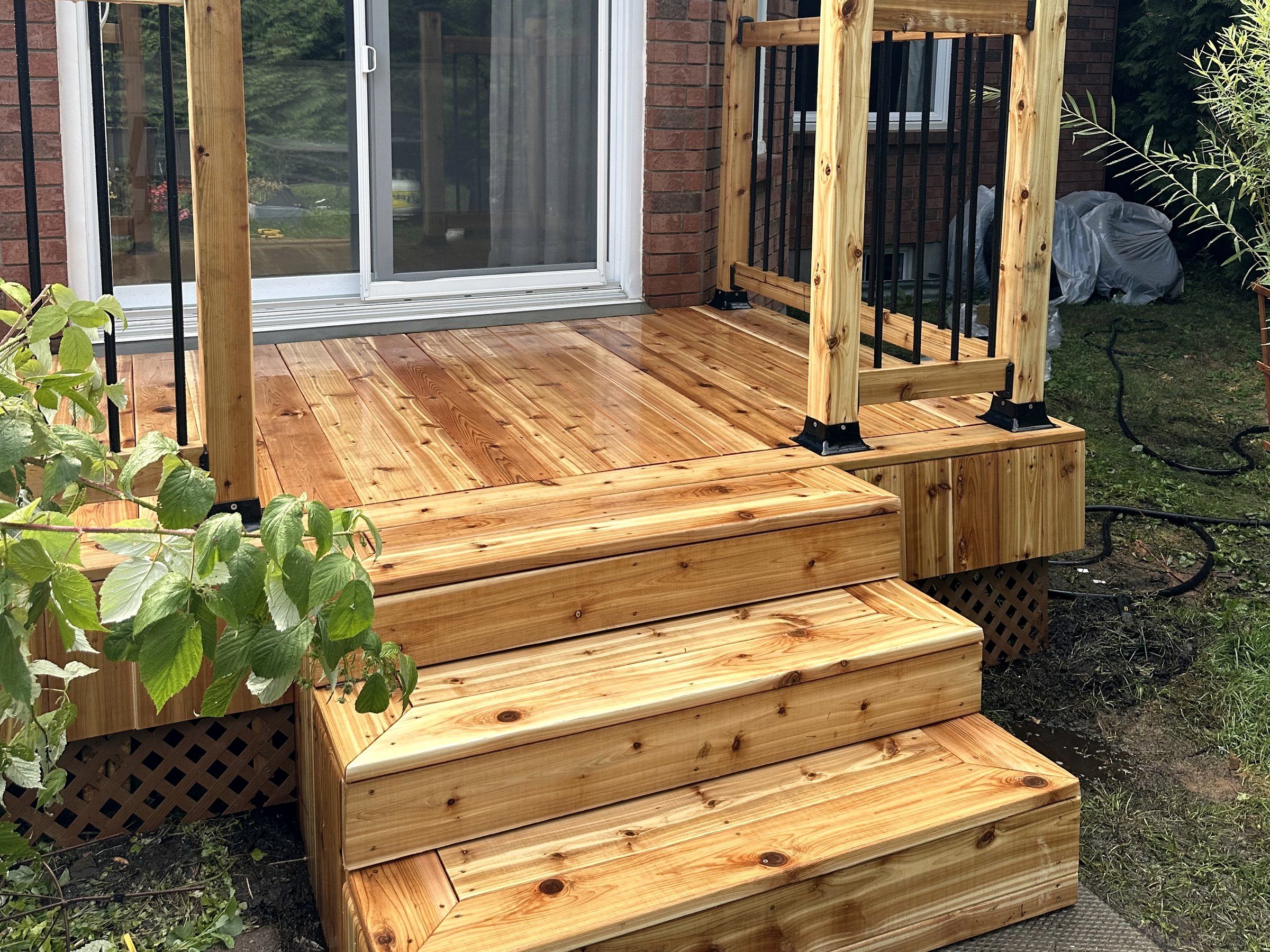 New cedar deck stairs with black aluminum balusters at a patio door