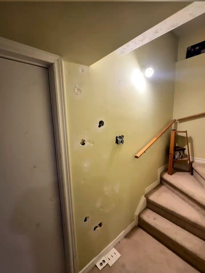 Basement wall at the foot of the stairs with holes and patched spots, before repair