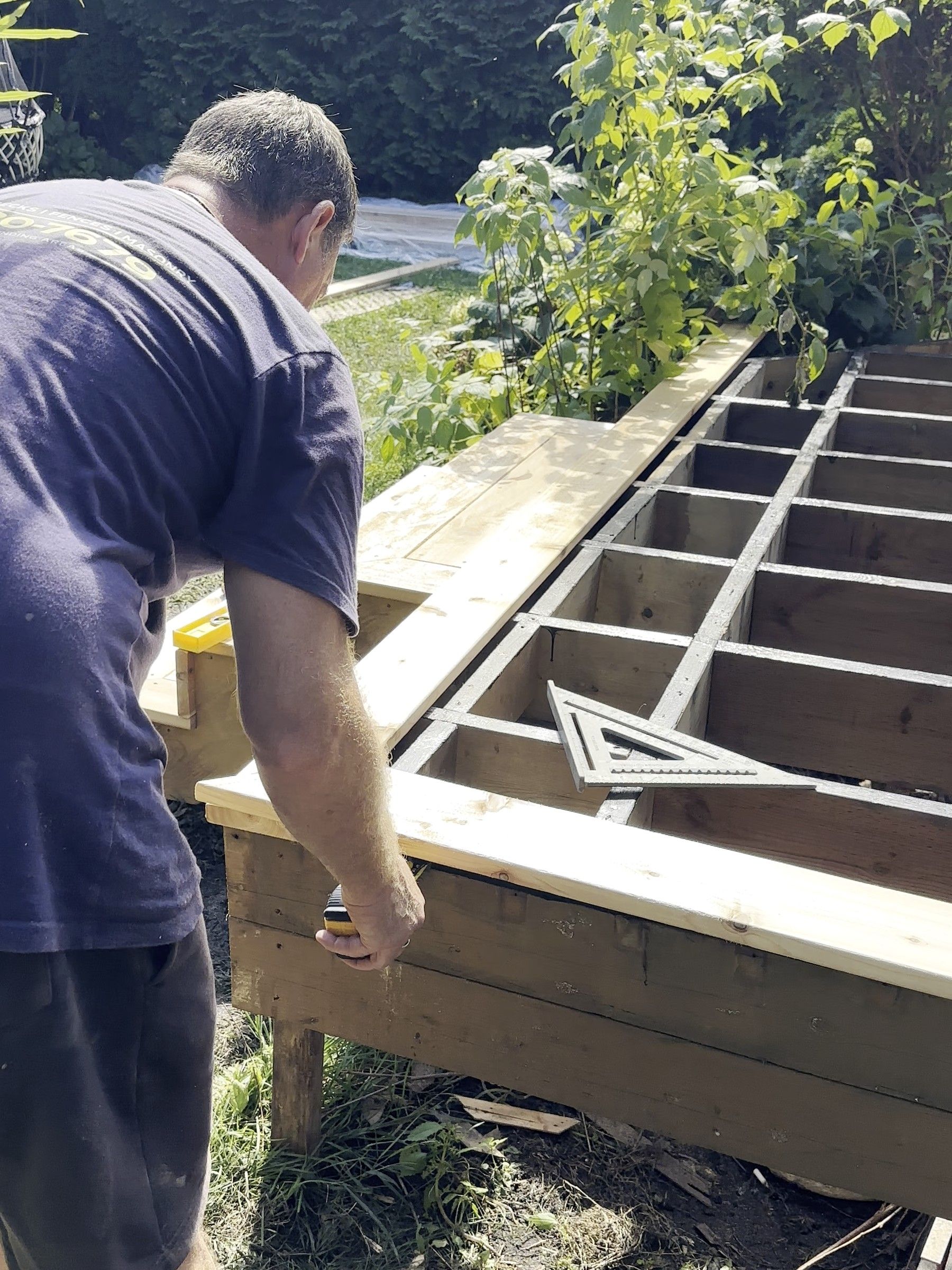 Korvex crew member checking a new pressure-treated deck frame with a speed square