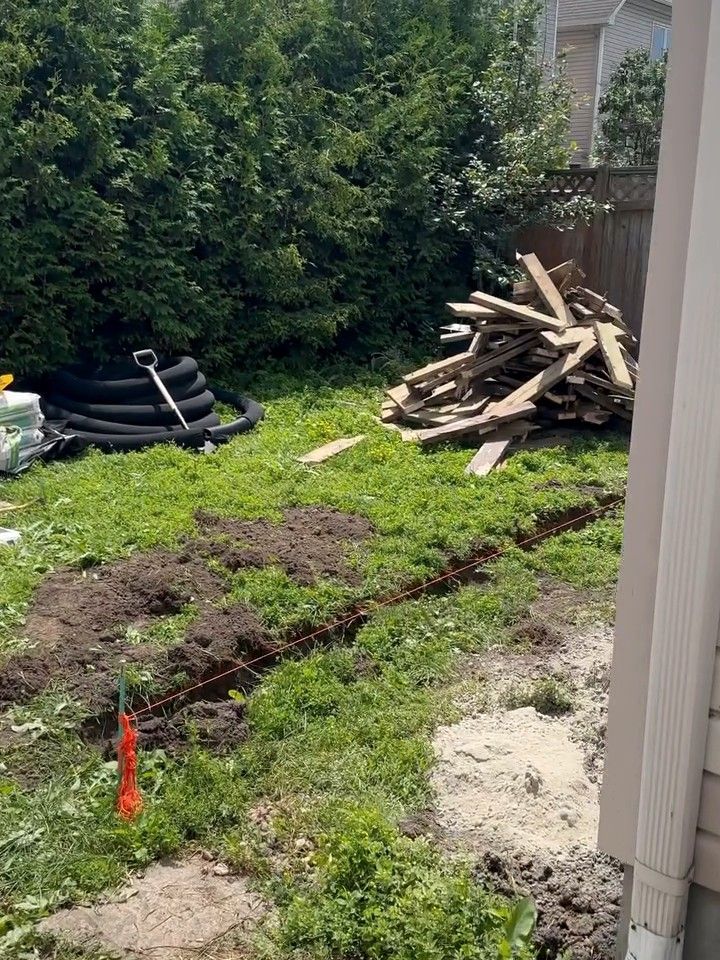 A French drain trench dug across a lawn, its line marked with flags