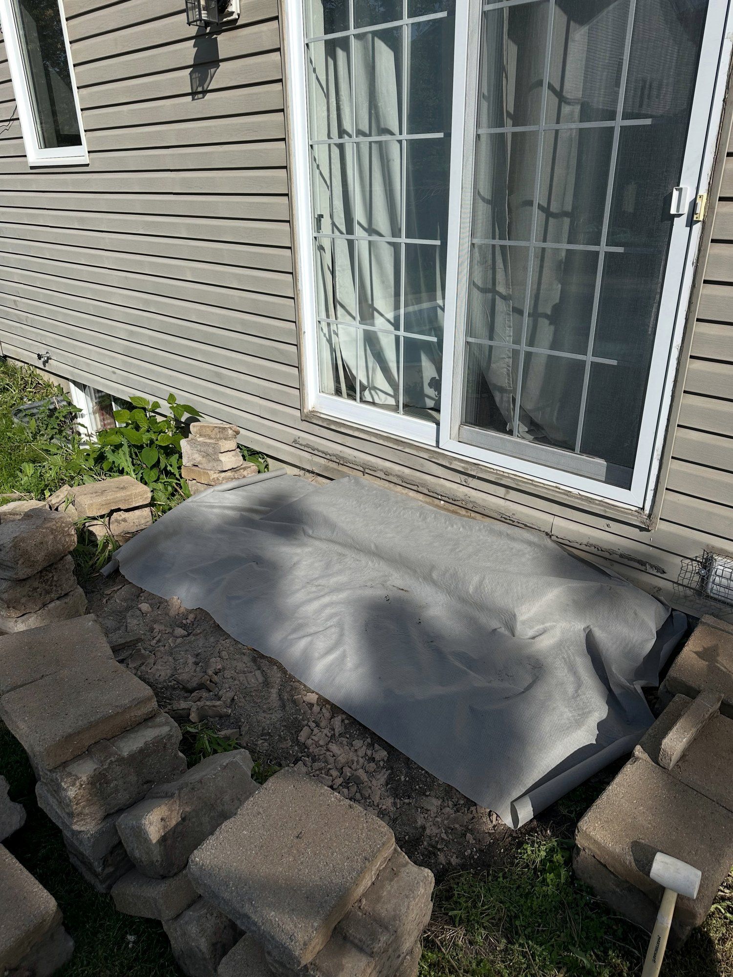 Old steps taken apart at a patio door, blocks stacked aside and fabric laid on the base