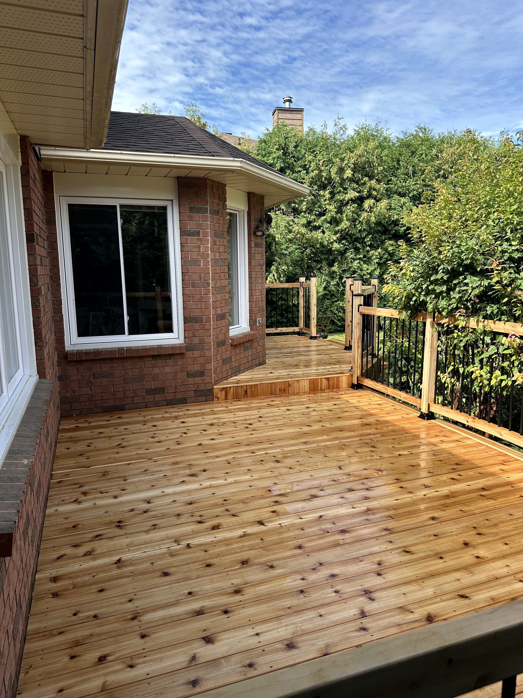 Rebuilt cedar deck with black aluminum balusters behind a brick house in Ottawa