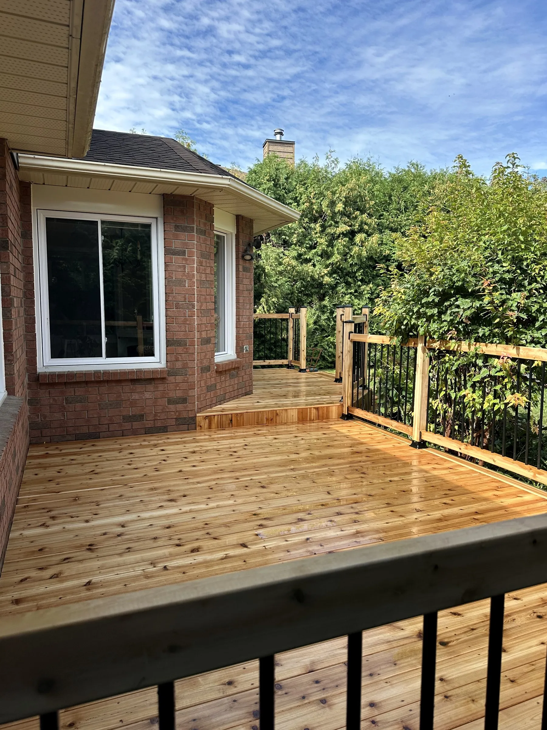 Rebuilt cedar deck with black aluminum balusters along a brick house