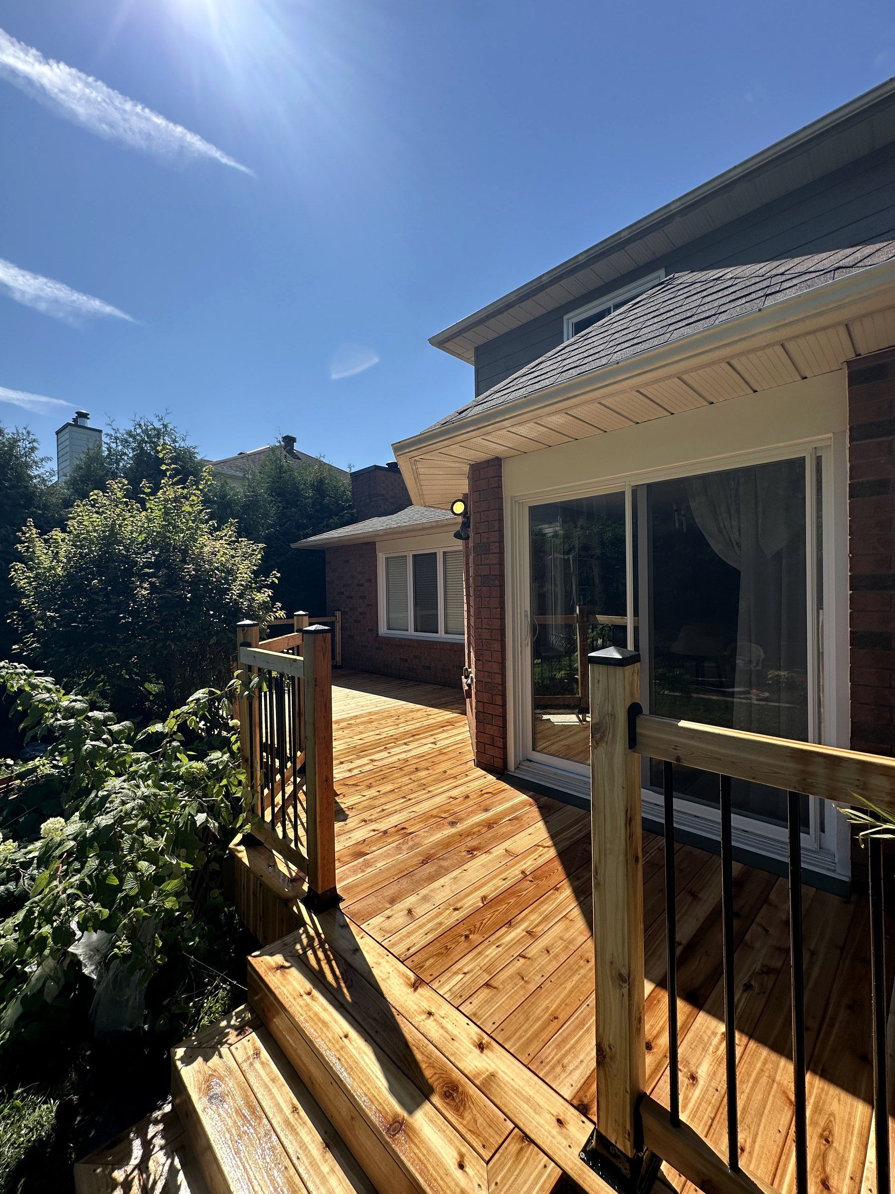 New cedar deck and stairs with black balusters along a brick house, rebuilt by Korvex in Ottawa