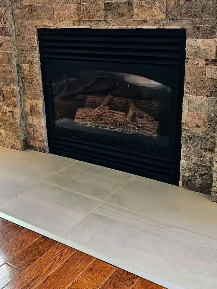 Gas fireplace refaced in stacked stone veneer, with a light tile hearth over a hardwood floor