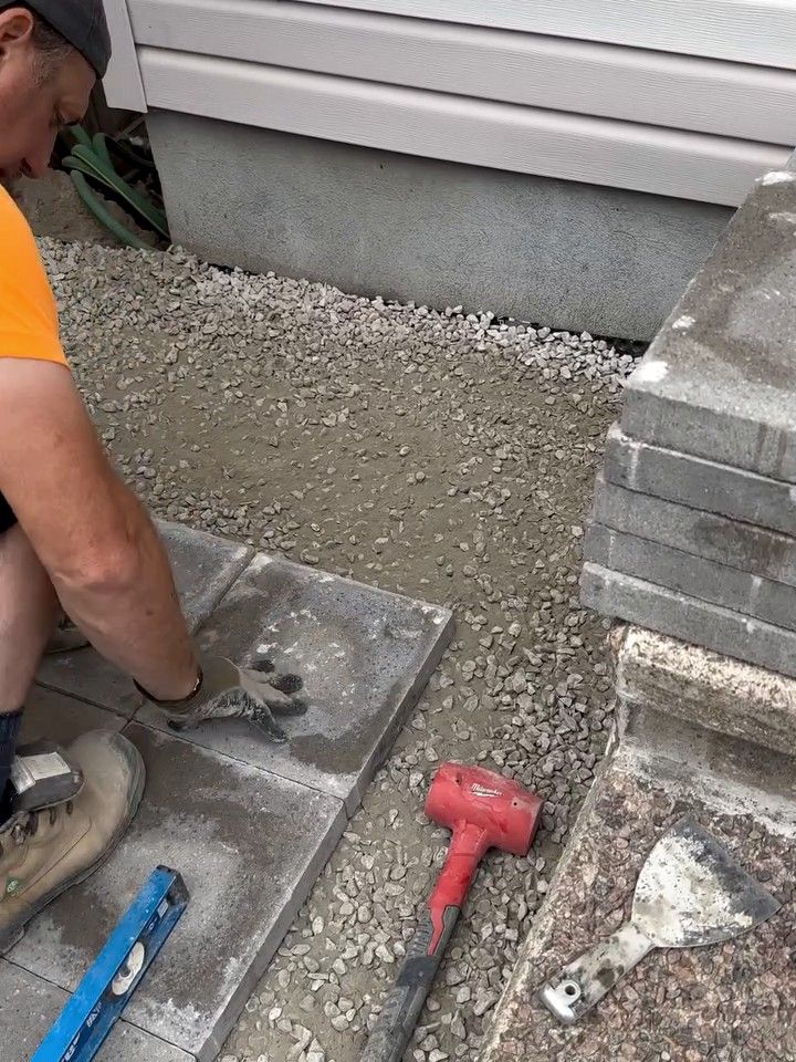 Korvex crew member setting a concrete slab on compacted stone, level and mallet beside it