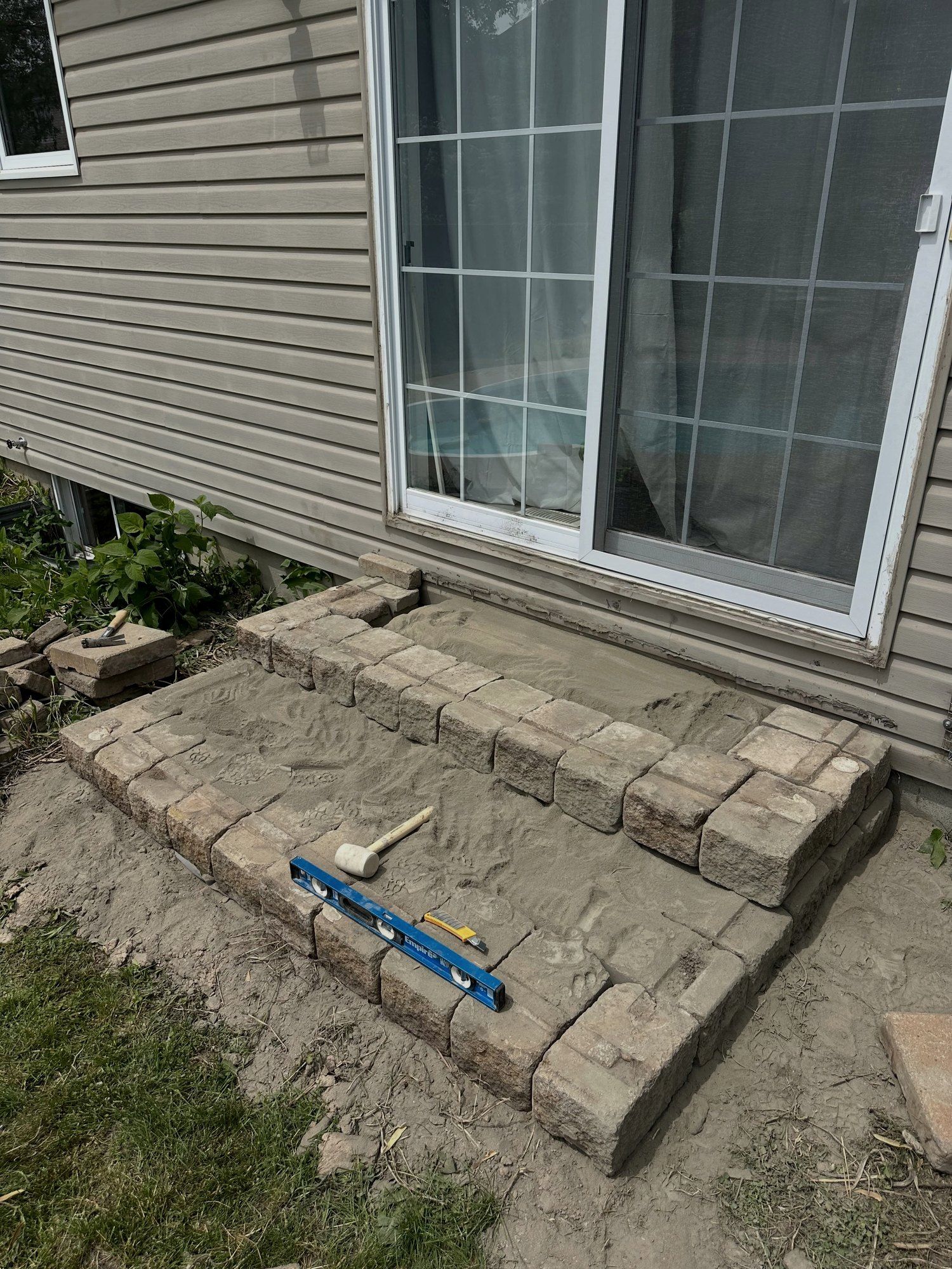 Segmental block steps being rebuilt at a patio door, a level resting across the new course