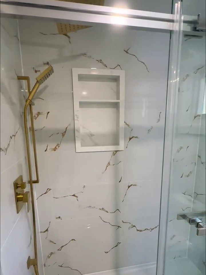 Tiled shower wall with a recessed niche and brushed-gold fixtures, behind a sliding glass door