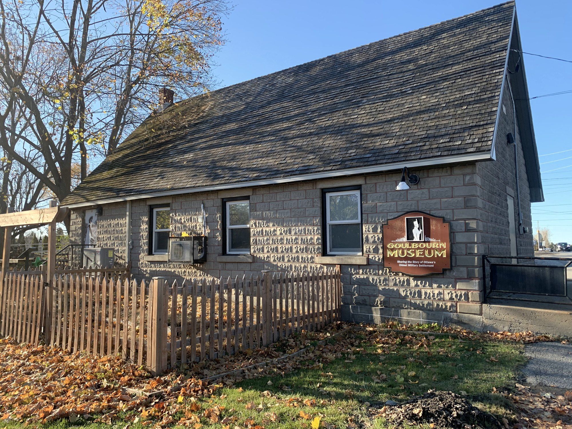 The stone Goulbourn Museum building with a picket fence and autumn leaves
