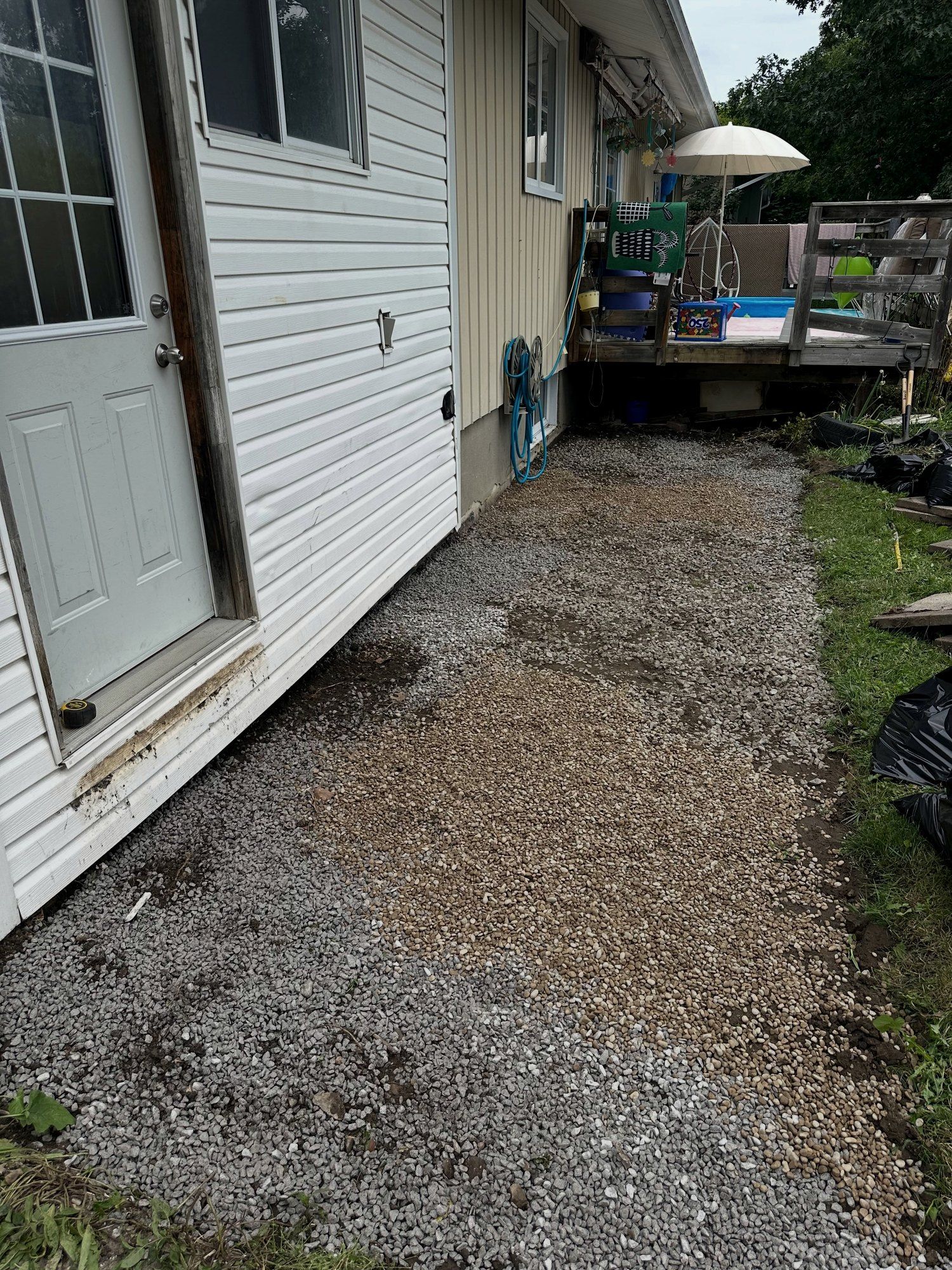 Clear-stone drainage strip along a house foundation in a side yard after old slabs were removed