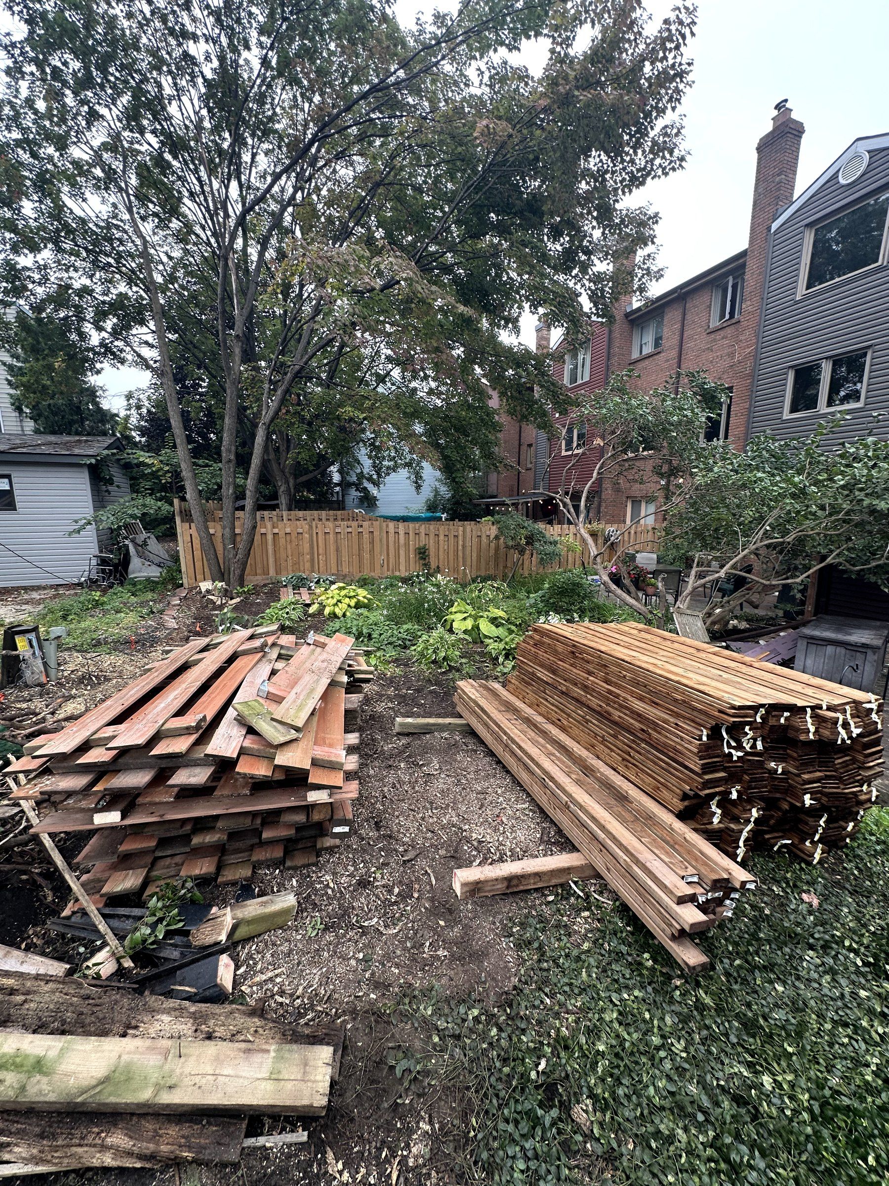 Old fence boards stacked in a yard next to new lumber, ready for the replacement