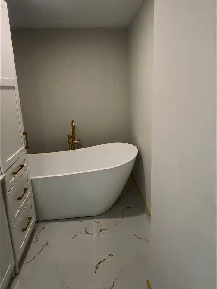 White freestanding tub with a floor-mounted filler on a marble-look tile floor