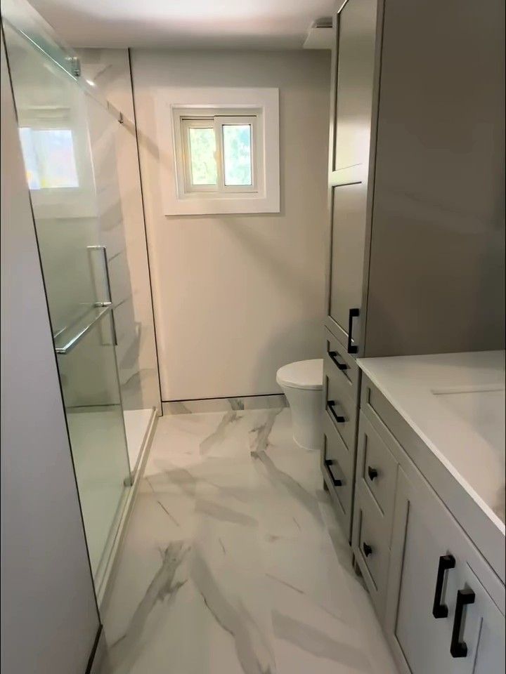 Marble-look tile floor running between a grey vanity and a glass shower