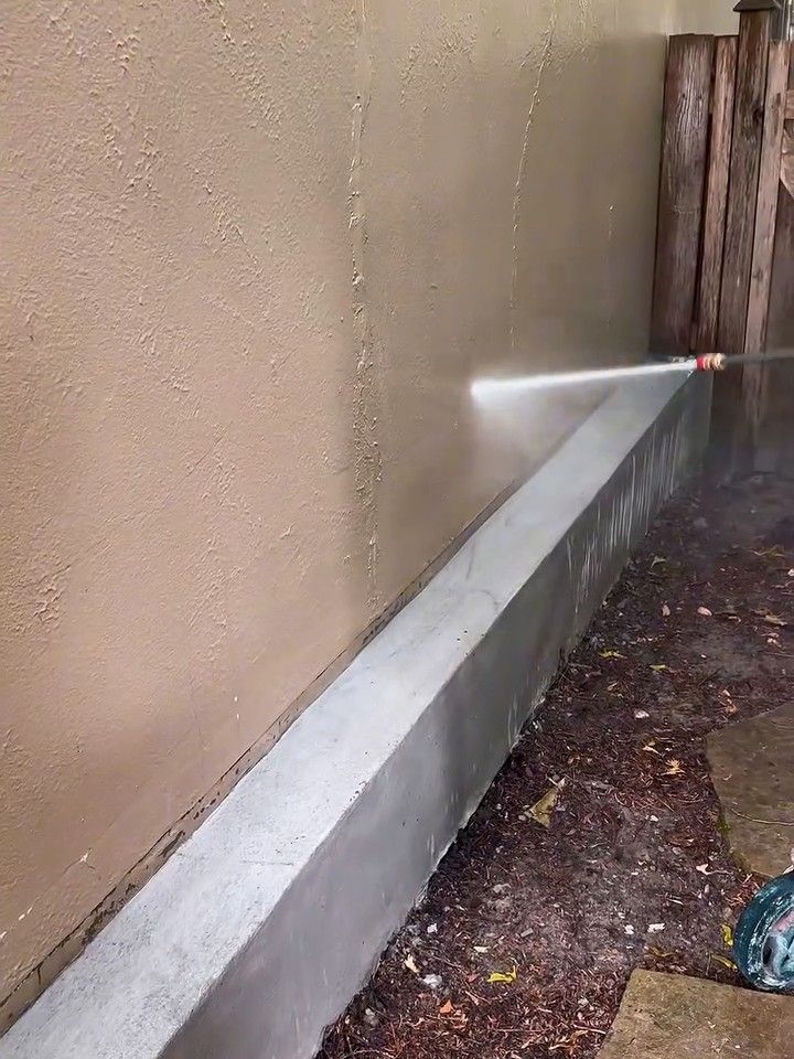 A stucco house wall being pressure-washed along its base
